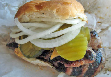 Charcoal-grilled sausage is piled into a bun with pickle chips and onions.