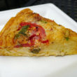 Bright yellow wedge of smoked gouda quiche shows herbs and tomato slice on top.