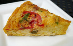 Bright yellow wedge of smoked gouda quiche shows herbs and tomato slice on top.