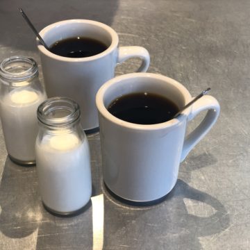 Two mugs of coffee, each with a tiny glass pitcher of chilled milk to add