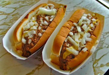 Two bunned hot dogs topped with chili, mustard, and chopped raw onions