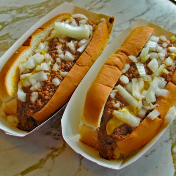 Two bunned hot dogs topped with chili, mustard, and chopped raw onions