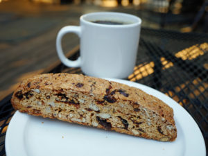 Hard, oblong biscuit crowded with cranberries and walnuts, with a cup of coffee