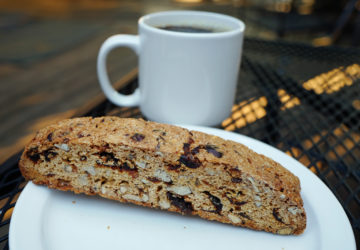 Hard, oblong biscuit crowded with cranberries and walnuts, with a cup of coffee