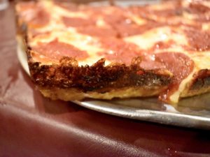 Corner of a thick pizza shows caramelized cheese on the crust.