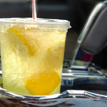 In a car cup-holder, plastic cup of lemonade reveals fresh lemon halves inside.