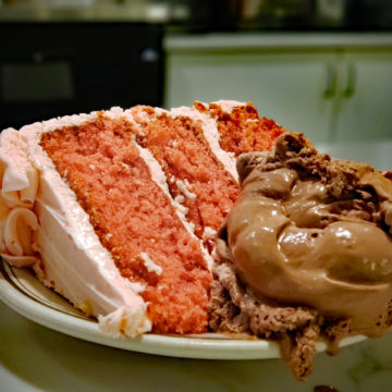 Pink, 3-layer strawberry cake is accompanied on its plate by a scoop of chocolate ice cream