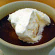 A crockery cup holds midnight-dark chocolate pudding topped with snowy-white whipped cream.