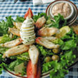 Large pieces of Dungeness crab are arrayed around a hard-boiled egg with lettuce and olives and a cup of dressing.