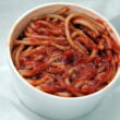 Large cup holds cooked spaghetti noodles dressed with crimson BBQ sauce