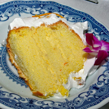Tender 3-layer orange-zested sponge cake, layered with custard, on fine china, boasts silky boiled frosting