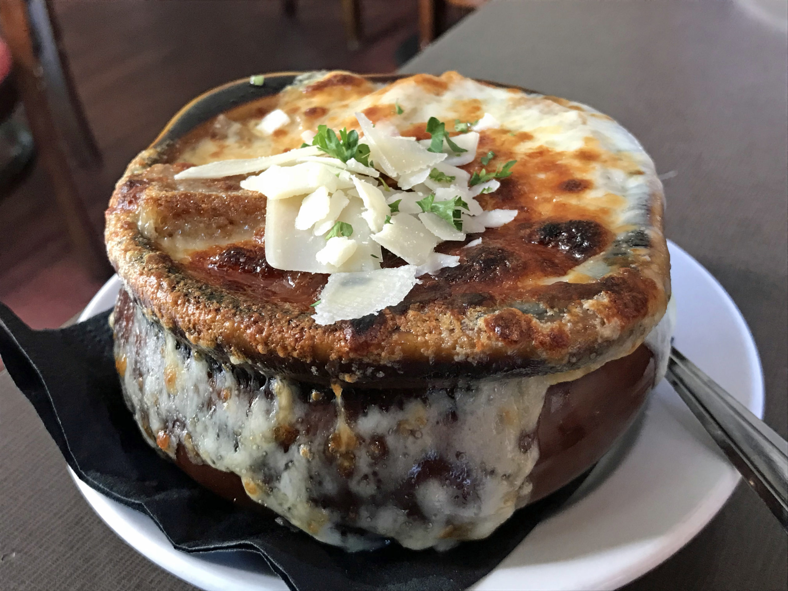 Molten cheese drips down the side of a crock of French onion soup.