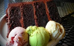 Scoops of strawberry, pistachio, and vanilla ice cream accompany a slice of 4-layer chocolate cake.