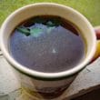 Cup of herb-speckled consomme on a screened porch
