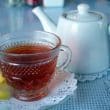 Hot tea in a glass cup with a pitcher for refills, on lacy paper doilies
