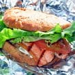 Grilled pink salmon fillet peeks out from a bun with lettuce and tomato garnishes