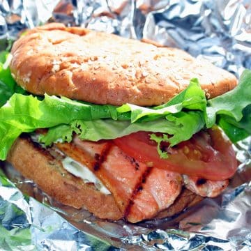 Grilled pink salmon fillet peeks out from a bun with lettuce and tomato garnishes