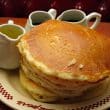 A plated stack of 5 hefty pancakes with pitchers of melted butter and syrup