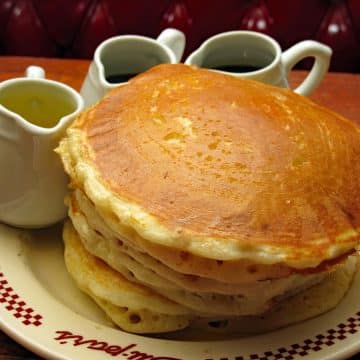 Stack of 5 pancakes with pitchers of syrup and melted butter