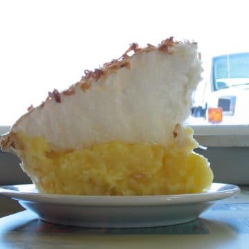 Wedge of pie with tall yellow base and even taller meringue, flecked with toasted coconut
