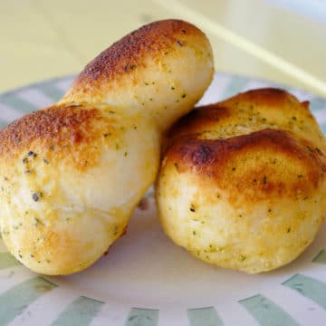Plate holds two herb-speckled, buttery knots of garlic bread
