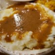 A great pile of mashed potatoes holds a spill of brown gravy.