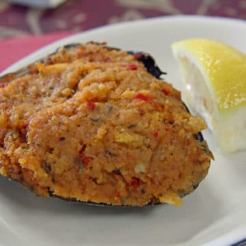 Clam shell stuffed with clam, sausage, and veggies, accompanied by a lemon for drizzling on