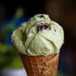 A scoop of pale green ice cream studded with chocolate chips tops an ice cream cone