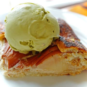A scoop of pale green pistachio ice cream crowns a slice of pear tart