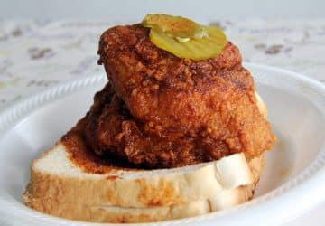 Meaty red-hued fried chicken breast atop two slices of white bread