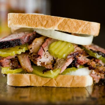 Smoke-cooked brisket piled into a sandwich with pickle chips and onions