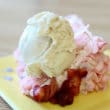 A scoop of vanilla ice cream crowns a piece of pink strawberry cake