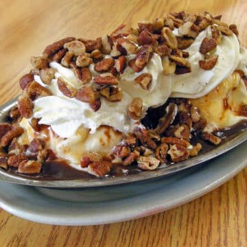 Long metal dish holds ice cream, syrup, chopped nuts, and whipped cream.