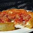 Sliced deep-dish pizza shows tomatoes, sausage, cheese in its wall of crust.