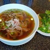 Bowl of beef pho with a plate of garnishes