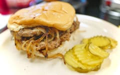 Double onion-fried burger on a plate with pickles