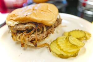 Double onion-fried burger on a plate with pickles